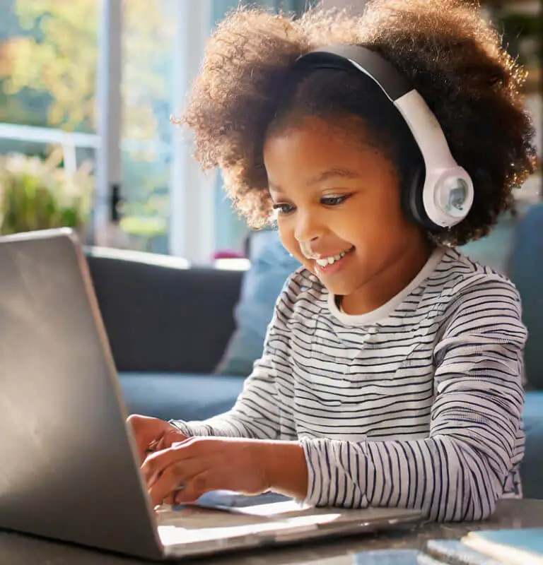 Smiling child wearing headphones using a laptop for online learning at home